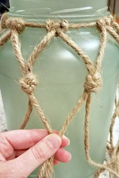 a hand is holding rope around a vase