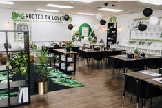 a room with tables, chairs and plants on the wall in front of it that says rooted in love