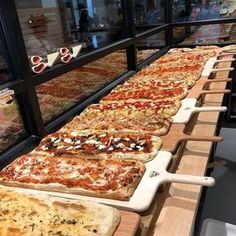 many pizzas are lined up on wooden trays in front of the glass window