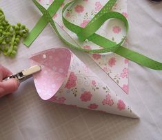 a person is cutting paper with scissors on a table next to flowers and green ribbon