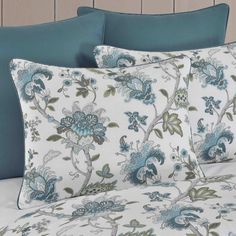 a bed with blue and green flowers on it's pillowcase, along with two pillows