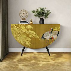 a sideboard with two cranes painted on it in front of a clock and plant