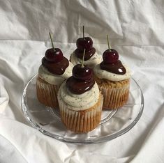 three cupcakes with cherries on top are sitting on a glass plate