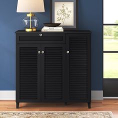 a black cabinet with shutter doors and a lamp next to it on top of a rug