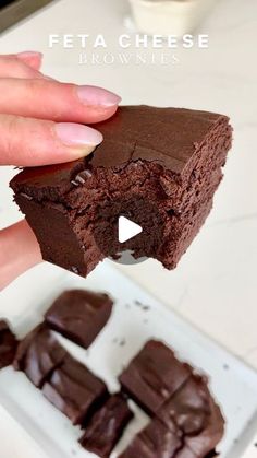 a person holding up a piece of chocolate brownie in front of some other pieces