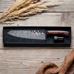 a knife in a black box on top of a wooden table next to some dry grass