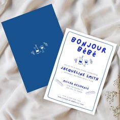 a blue and white wedding card sitting on top of a bed next to some flowers