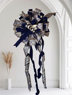 a large blue and gold bow hanging from the side of a white wall next to a vase