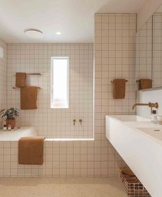 a bathroom with white tile and tan towels on the wall, along with two sinks