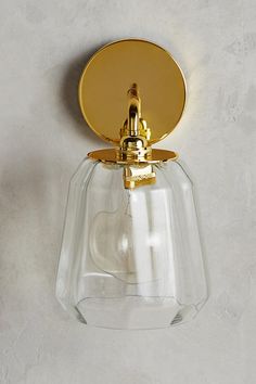 a wall light that has a glass shade on the side and gold trim around it