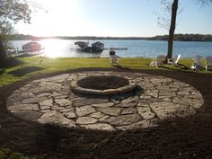 a stone fire pit in the middle of a grassy area next to a body of water