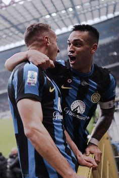 two men standing next to each other in front of a soccer field with their arms around each other