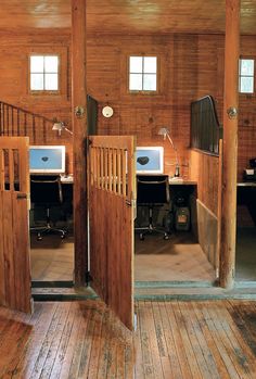 two computers sitting on top of wooden desks in an open area with stairs leading up to them