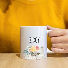 a woman holding a white coffee mug with a cat on it's side and the word ziggy written in black