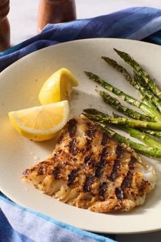 grilled fish and asparagus on a plate with lemon wedges next to it