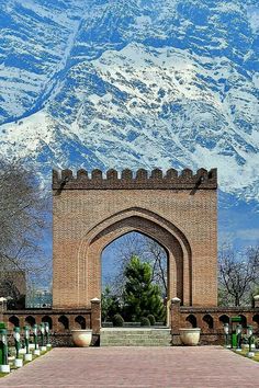 an arch in the middle of a brick walkway leading to a mountain range with snow on it