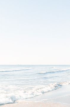 a person walking on the beach with their surfboard in hand and water behind them