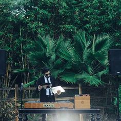 a man standing in front of a keyboard on top of a wooden table next to trees