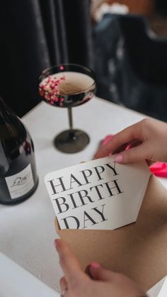 a woman holding a piece of paper with the words happy birth day on it next to a bottle of wine