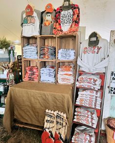 an assortment of shirts and other items on display in a market stall, including t - shirts