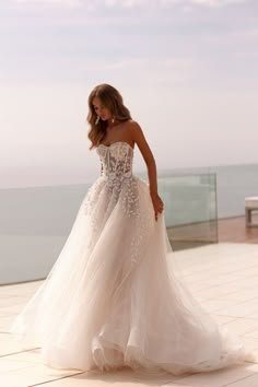 a woman in a wedding dress is standing on the balcony looking at the ocean with her back to the camera