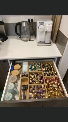 an open drawer in a kitchen filled with coffee cups and other items on the counter