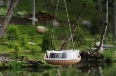 a swing chair hanging from the side of a body of water with trees in the background