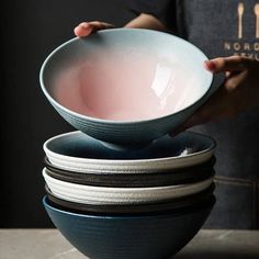 a person holding a bowl in front of several bowls stacked on top of each other