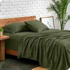 a bed with green sheets and pillows in a room next to a potted plant