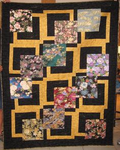 a woman holding up a quilt made with flowers and black squares on the front, yellow border