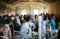 a group of people sitting at tables in a room with lights hanging from the ceiling