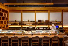 a chef preparing food in a restaurant with lots of wooden tables and chairs around it