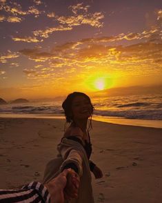 two people are holding hands on the beach at sunset, with the sun setting in the background