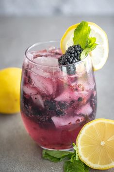 a glass filled with ice and blackberries next to lemons