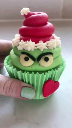 a hand holding a green cupcake with red and white frosting