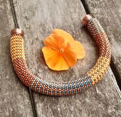 an orange flower sitting on top of a wooden table next to a beaded bracelet