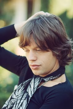 a young man wearing a black shirt and neck tie with his hands on his head