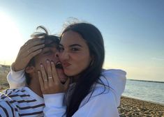 a man and woman on the beach with their hands around each other's faces