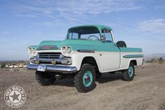 an old green and white truck parked in the dirt