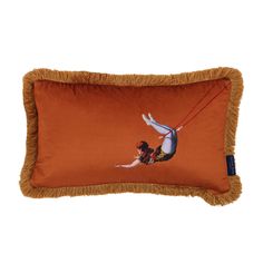 an orange pillow with a woman on a swing in the air and fringe trimmings