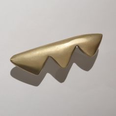 a close up of a gold metal object on a white surface with a shadow from it