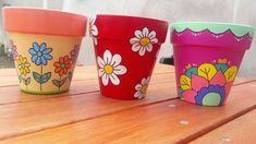 three colorful flower pots sitting on top of a wooden table with flowers painted on them