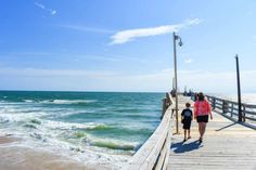 two people walking down a pier towards the ocean