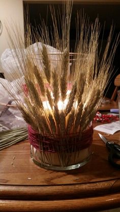 a glass vase filled with lots of dry grass sitting on top of a wooden table