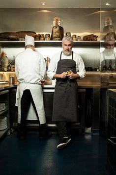 two men in aprons are standing at the counter and one is looking at something