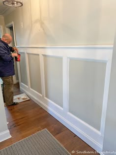 an older man is painting the walls in his living room with white paint and wood flooring