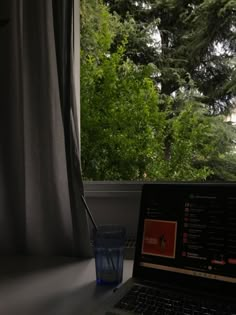 an open laptop computer sitting on top of a desk next to a window with trees outside