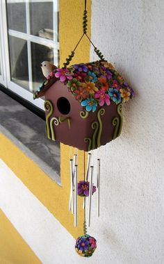 a bird house hanging from the side of a building with flowers on it's roof