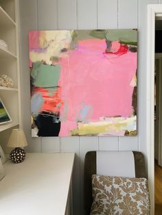 an abstract painting hangs on the wall above a white desk with a chair and lamp