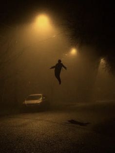 a person jumping up in the air on a foggy street at night with cars passing by